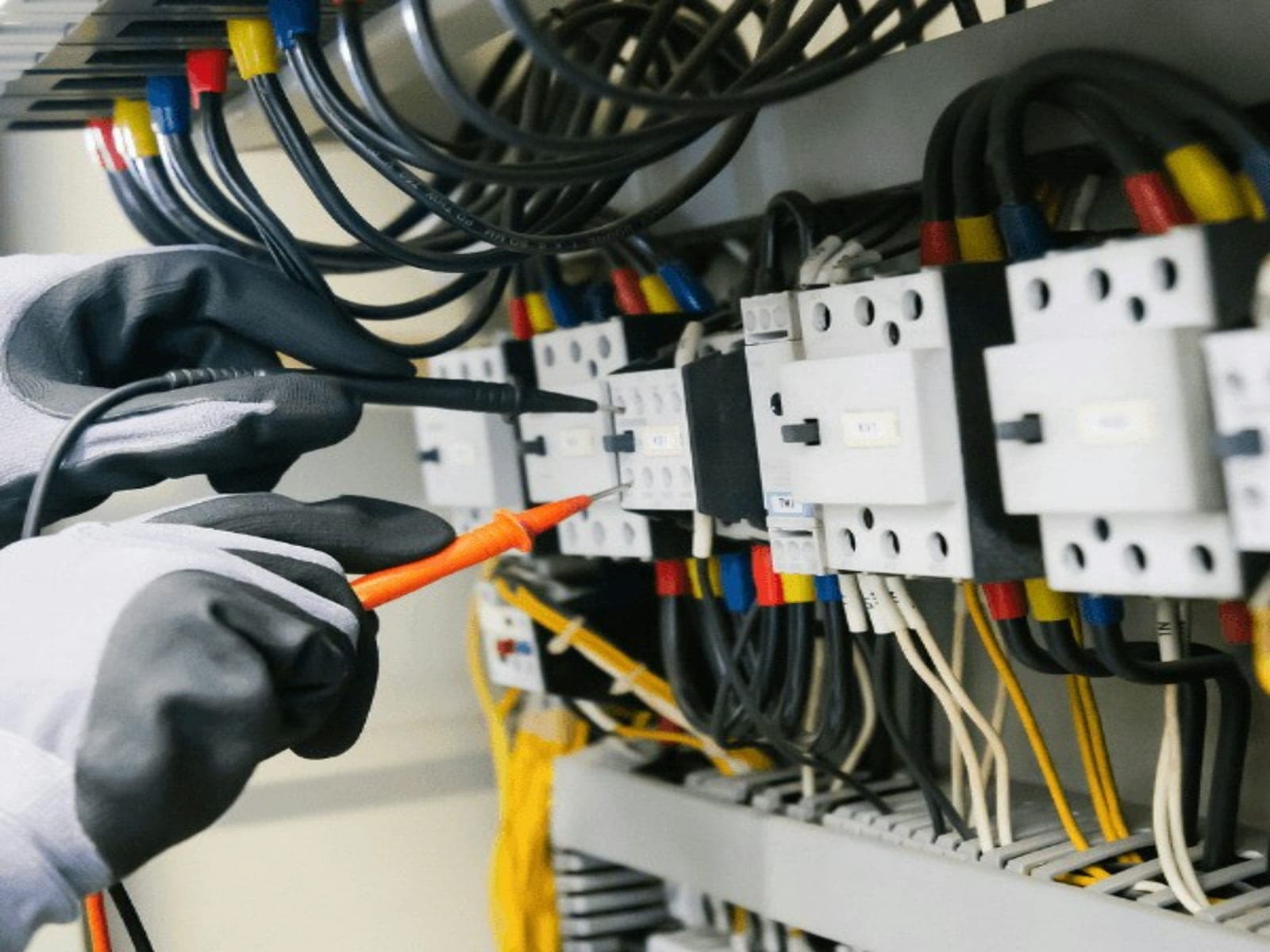 A Cape Current electrician testing contactors in a distribution board with a multimeter